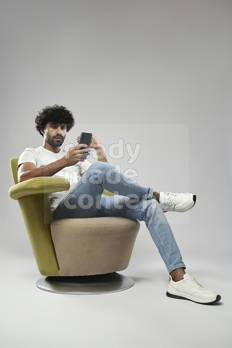 A man wearing casual sitting on a chair browsing on the phone on white background