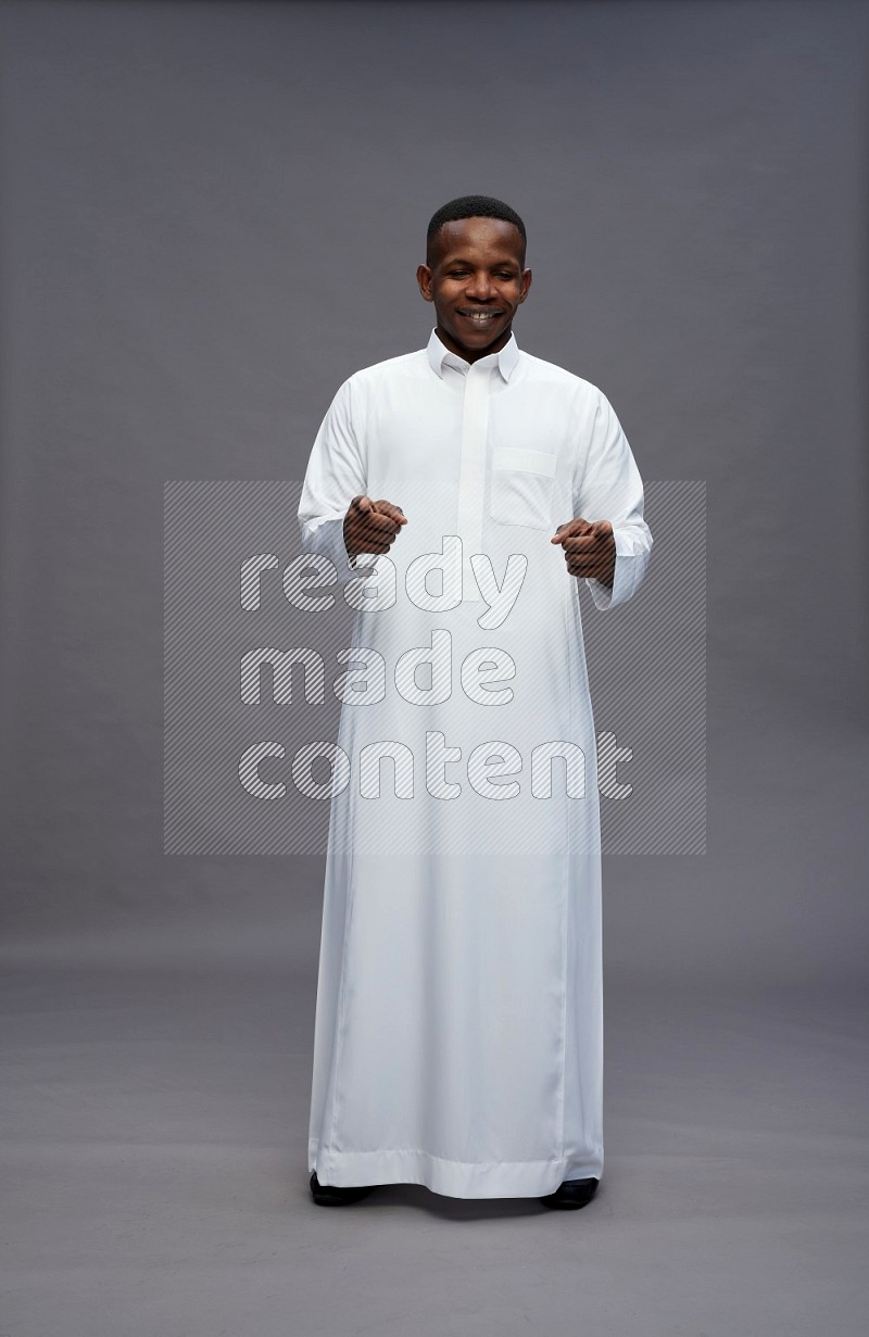 Saudi man wearing thob standing interacting with the camera on gray background