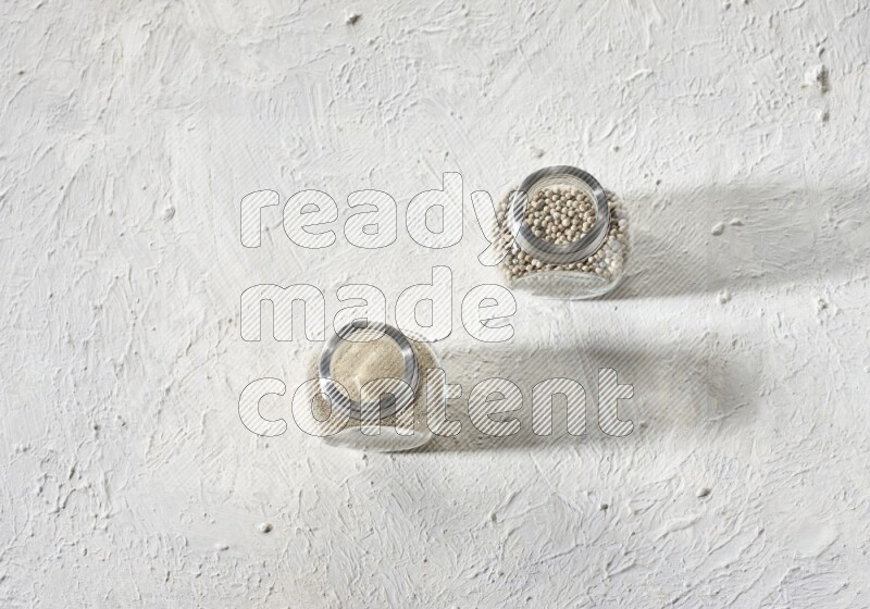 وعاءين زجاجيين عشبيين ممتلئين بحبوب وبودرة الفلفل الأبيض على أرضية بيضاء