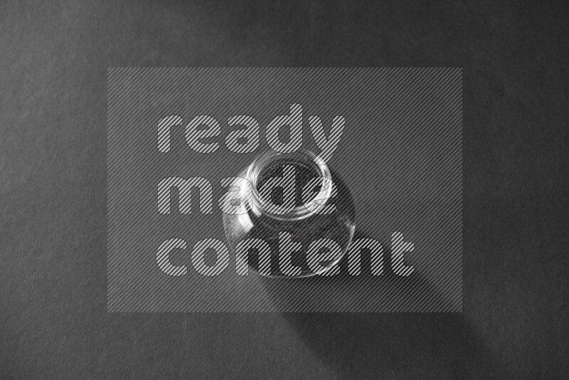 A glass spice jar full of black seeds on black flooring