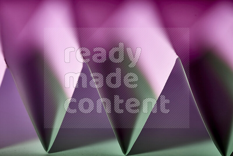 A close-up abstract image showing sharp geometric paper folds in green and purple gradients
