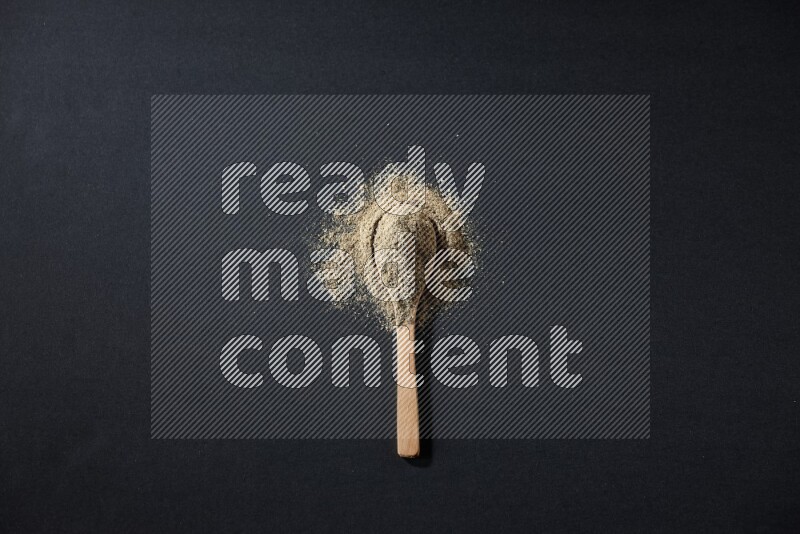 ملعقة خشبية ممتلئة ببودرة الهيل والبودرة تناثرت على خلفية سوداء