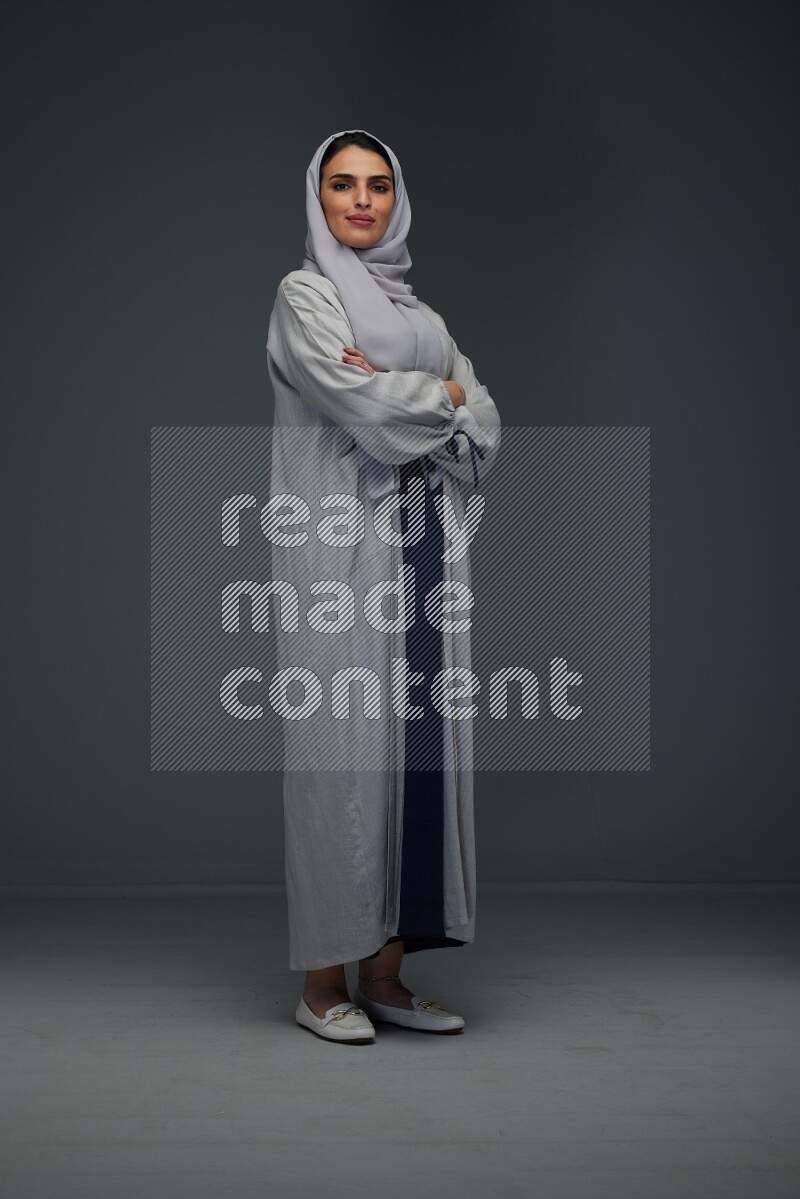 A Saudi woman wearing a light gray Abaya and head scarf standing and making multi poses eye level on a grey background