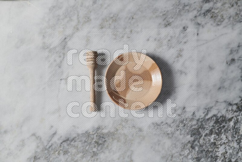 Multicolored pottery plate with wooden honey dipper on the side on grey marble background