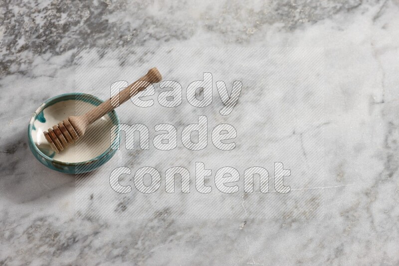 Multicolored pottery bowl with wooden honey dipper in it on grey marble background
