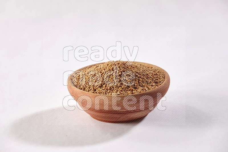 A wooden bowl full of mustard seeds on a white flooring