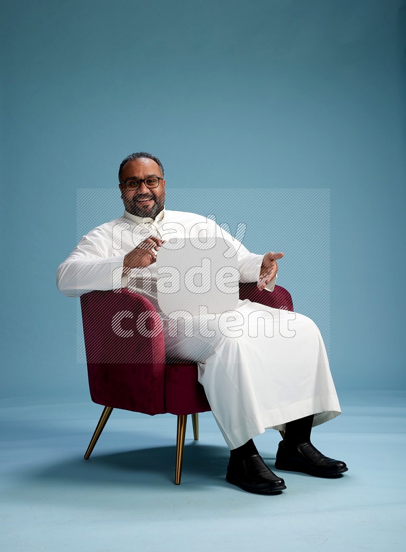 Saudi Man without shimag sitting on chair holding social media sign on blue background