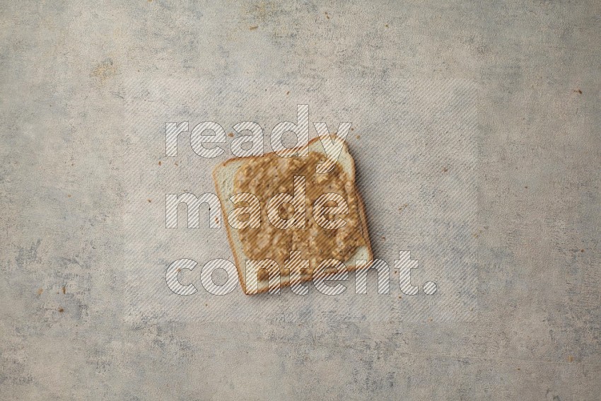 Crunchy peanut butter on a white toast on a light blue textured background