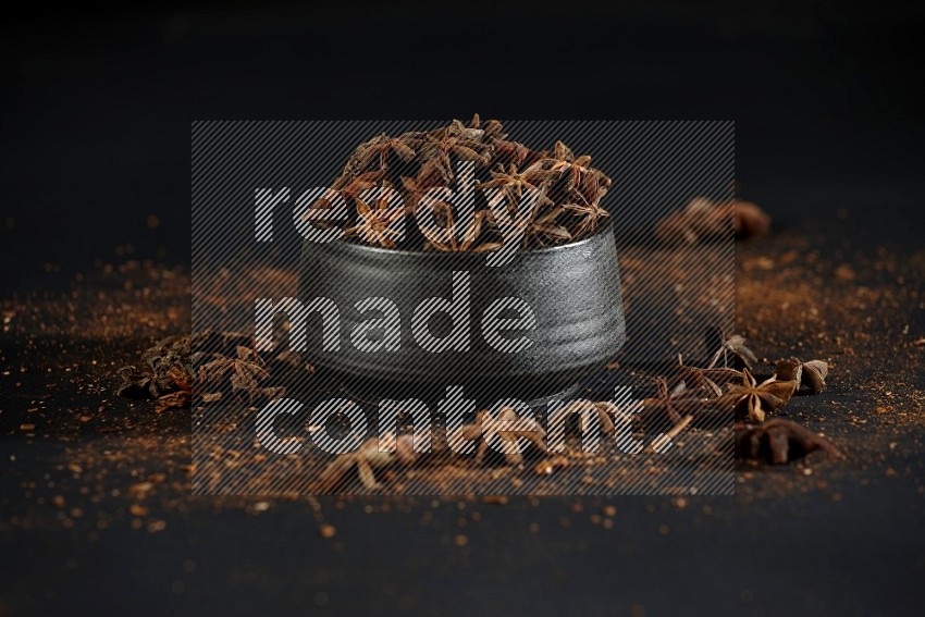 Star Anise herb in a black bowl with sprinkled herbs on black flooring