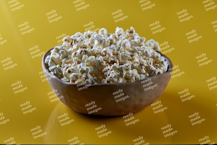 A brown pottery bowl full of popcorn on a yellow background in different angles