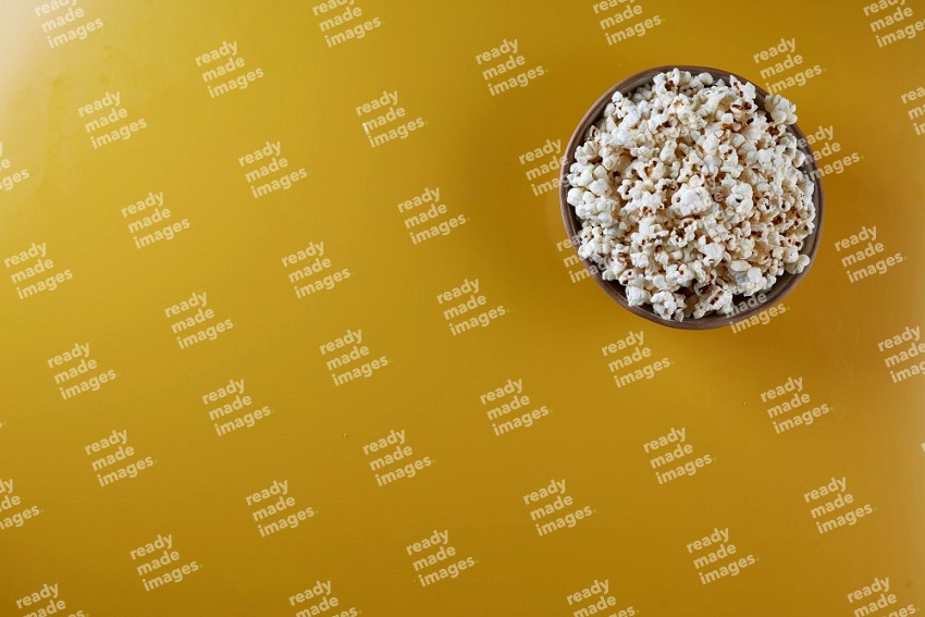 A brown pottery bowl full of popcorn on a yellow background in different angles