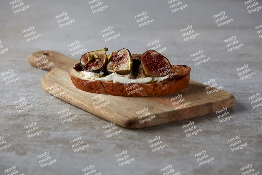 figs halves with cream cheese on toasted sourdough slice on a wooden board on textured grey background