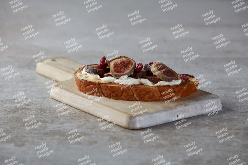 figs slices  with cream cheese on toasted sourdough slice on a wooden board on textured grey background