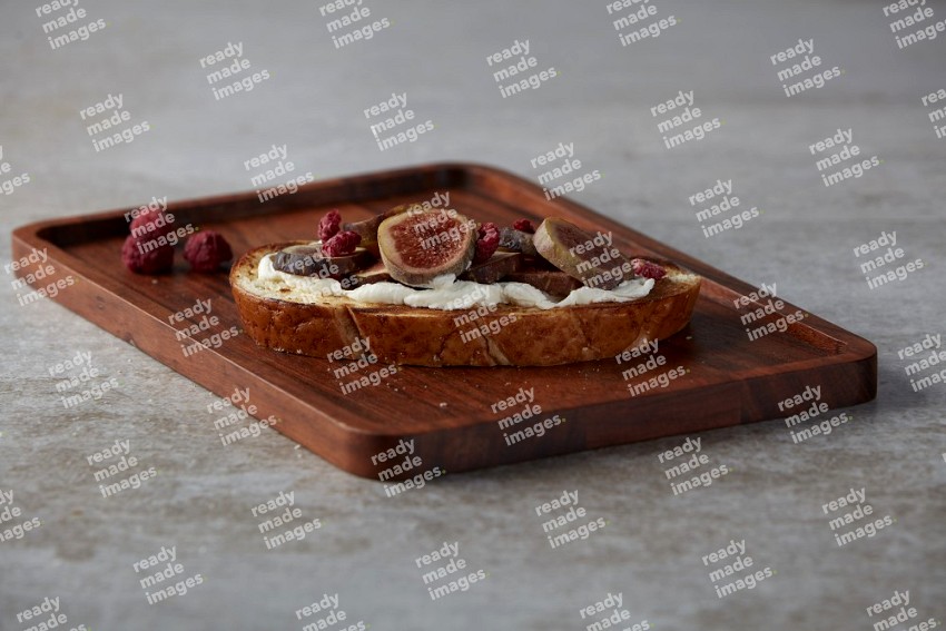 figs slices  with cream cheese on toasted sourdough slice on a wooden board on textured grey background