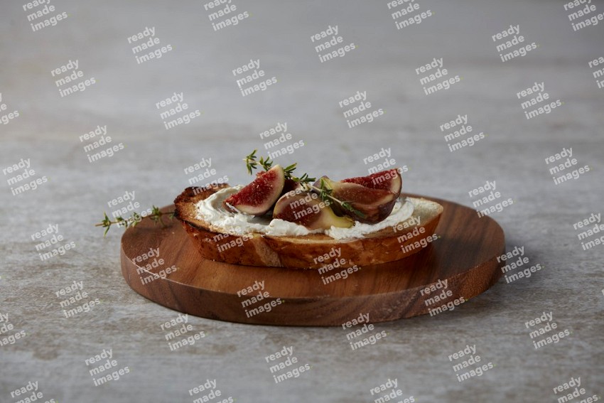 quarters of figs with cream cheese on toasted sourdough slice on a wooden board on textured grey background