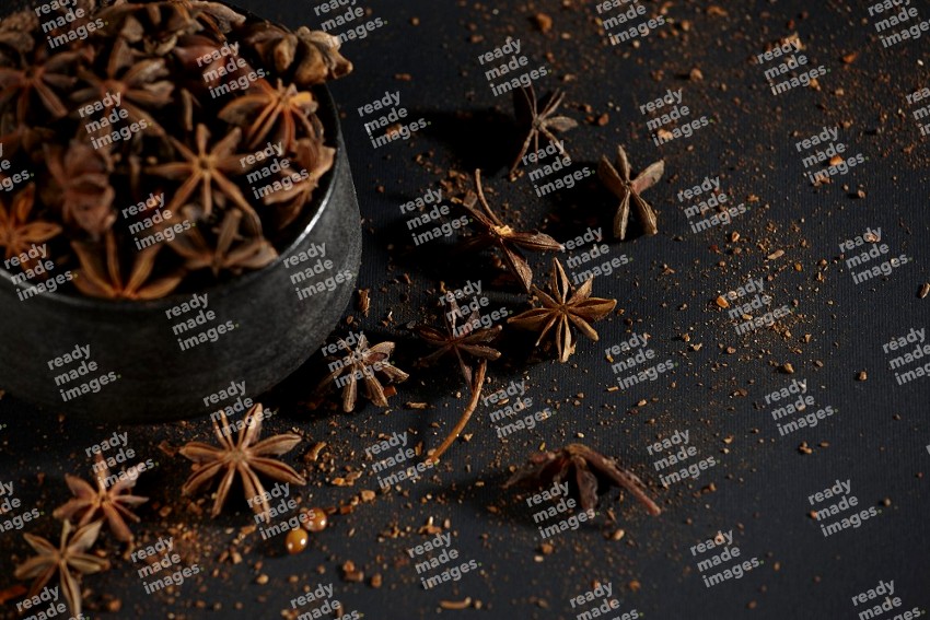 Star Anise herb in a black bowl with sprinkled herbs on black flooring