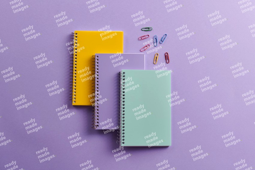 Multicolored notebooks with school supplies on purple background (Back to school)