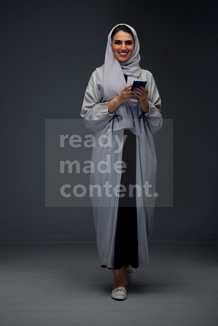 A Saudi woman Texting wearing Grey Abaya on a grey background