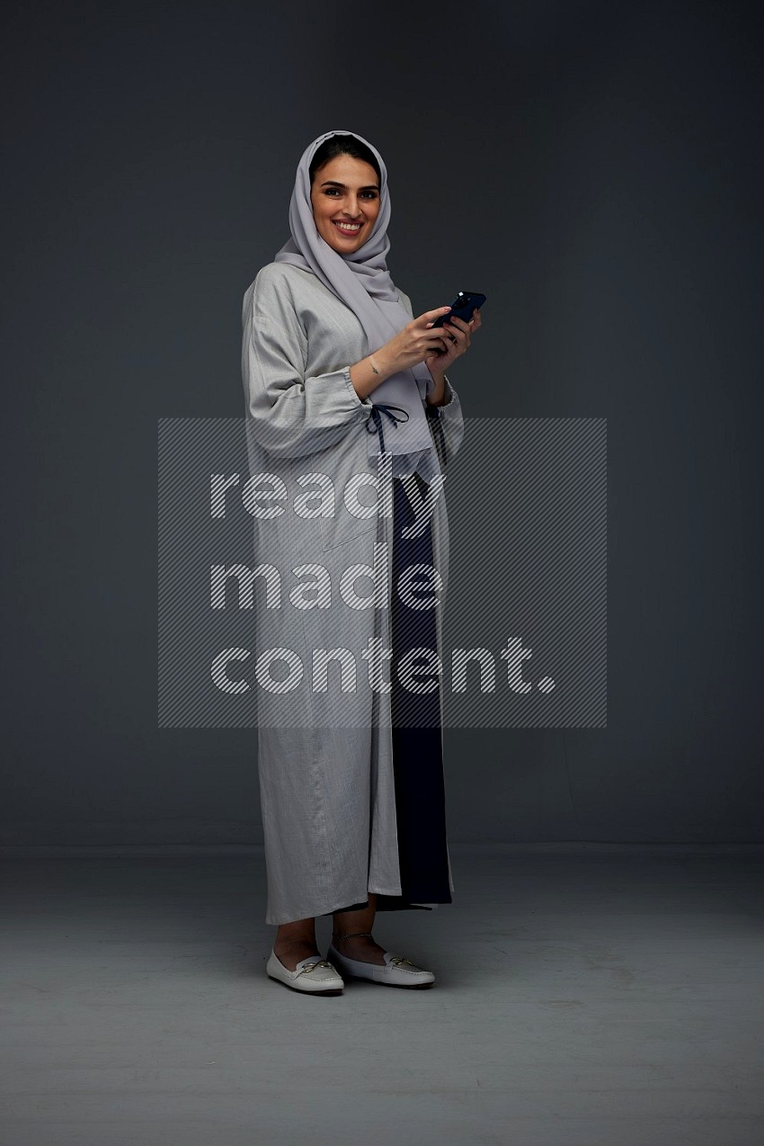A Saudi woman Texting wearing Grey Abaya on a grey background
