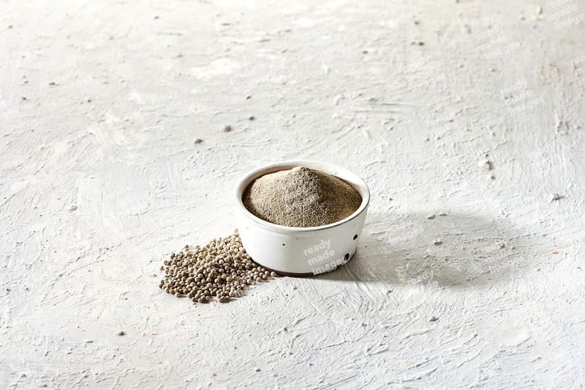 white pottery bowl full of white pepper powder with white pepper beads on textured white flooring